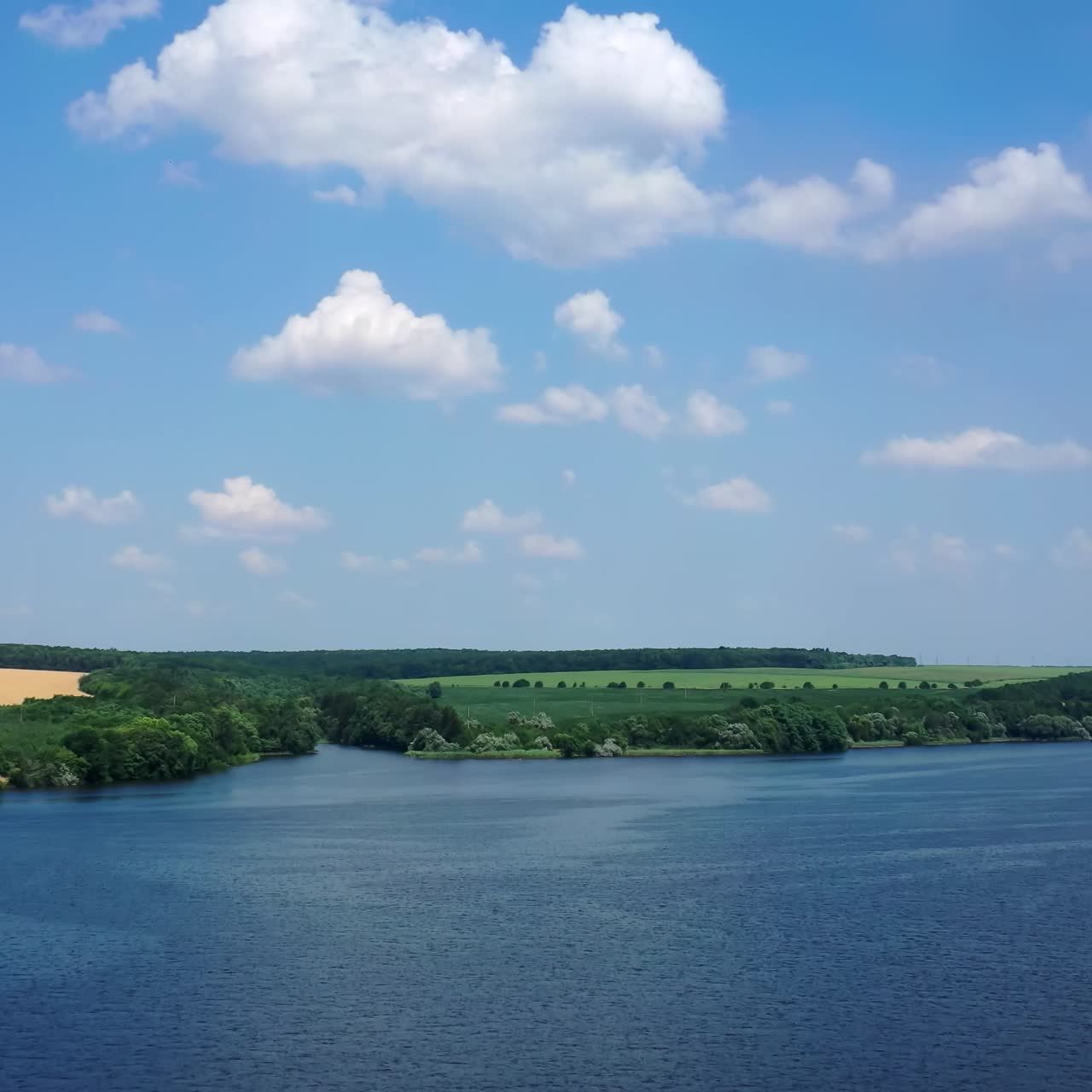 Tranquil atmosphere of summer nature. Flight over the beautiful blue river under the sky. Clean lake landscape on green fields background. Aerial view