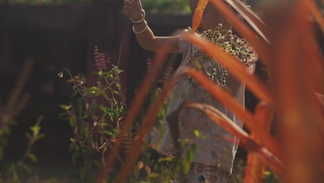 Low-angle-handheld-shot-of-a-girl-standing-in-garden-with-various-plants-holding-flowers-in-her-hands-while-throwing-a-plant-on-the-ground