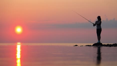 Frau-Fischt-Auf-Angelrute,-Die-Sich-Bei-Sonnenuntergang-Im-Hintergrund-Dreht.