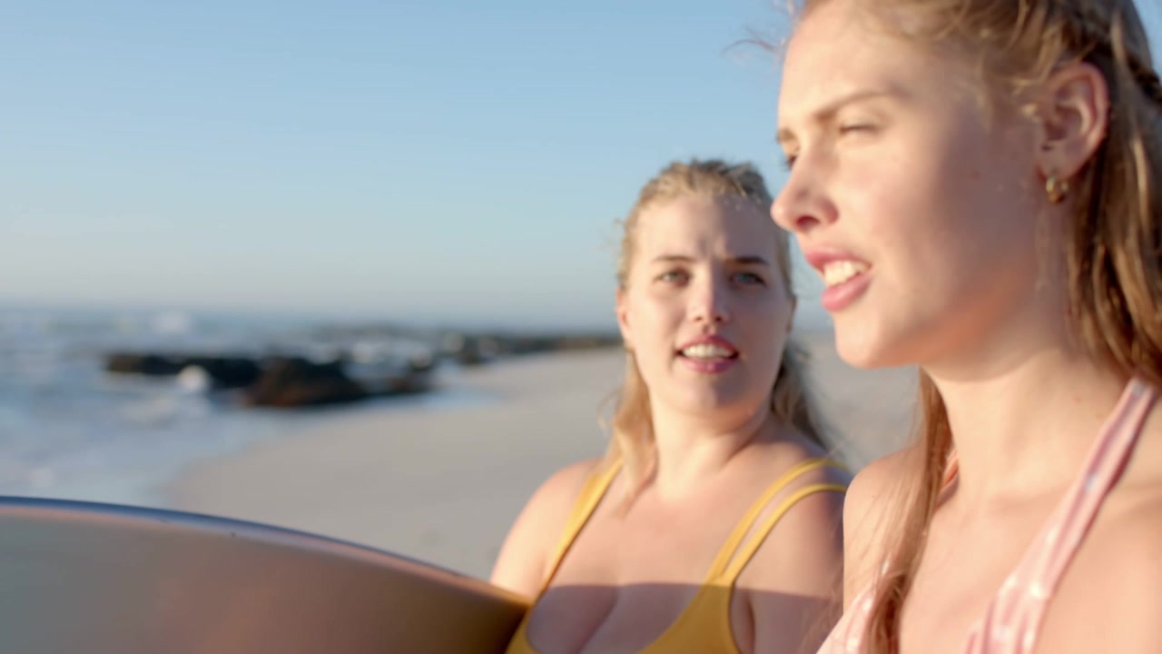Due donne che discutono di surf in spiaggia, la telecamera si avvicina, archi al neon scorrono sulla tavola per il design.