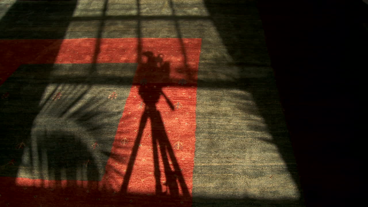 абстрактный концептуальный снимок, рассматривающий тень, созданную пленочной камерой на штативе, движущейся в тени в режиме time lapse