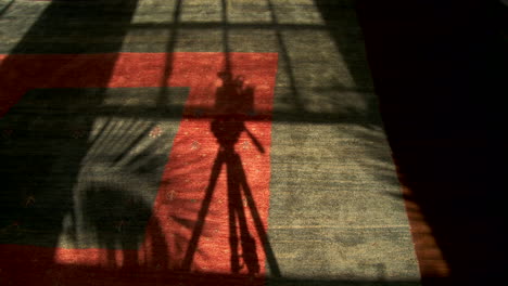 an abstract conceptual shot looking at the shadow made by a film camera on tripod moving in shadow in time lapse