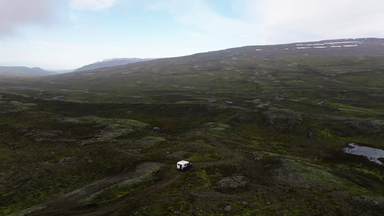 Drone orbiting a overlanding truck, driving in mossy highlands of cloudy Iceland