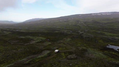 drone orbiting a overlanding truck, driving in mossy highlands of cloudy iceland