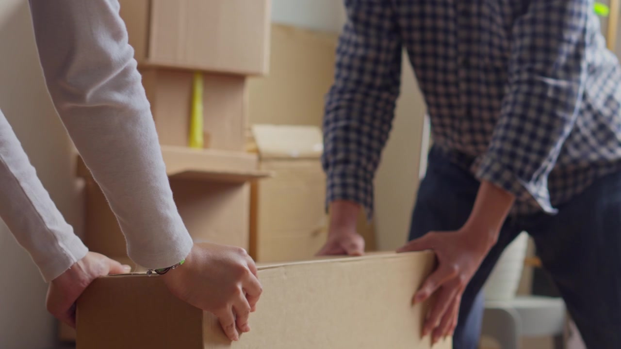 Close-up shot of hands coordinating to pick up and move heavy box during relocation