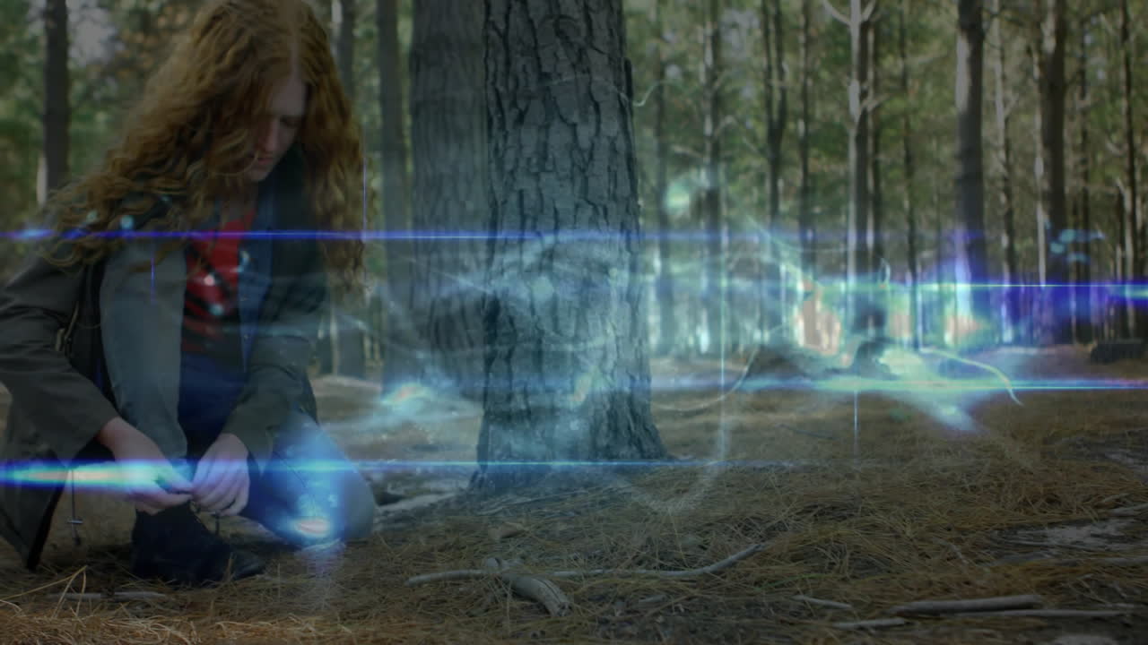 female designer crouching in pine forest clearing, interacting with blue energy lines for tech