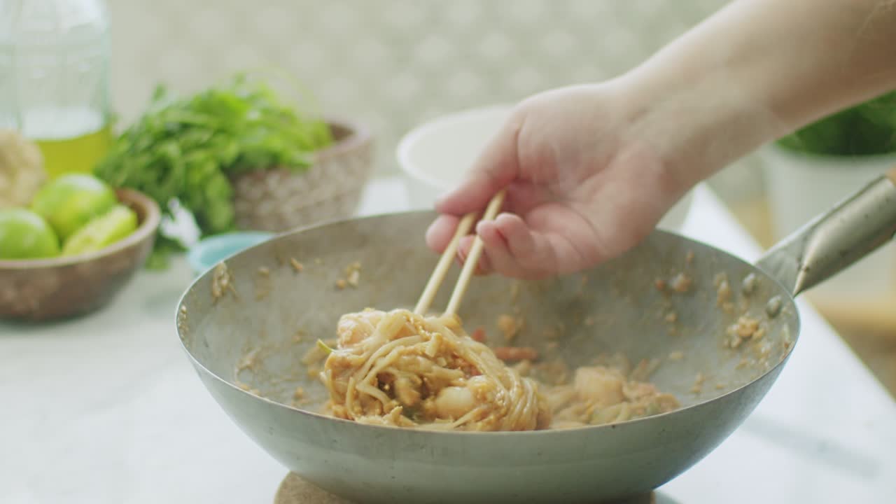 Woman stirring hot wok noodles with chopsticks