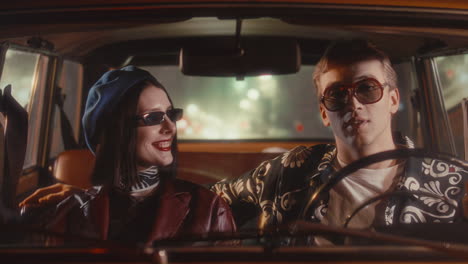stylish couple chatting and laughing in vintage car during night drive