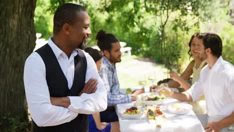 waiter standing with arms crossed while couples interacting in background