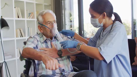 Video-of-biracial-female-doctor-in-face-mask-keeping-oxygen-to-caucasian-senior-man