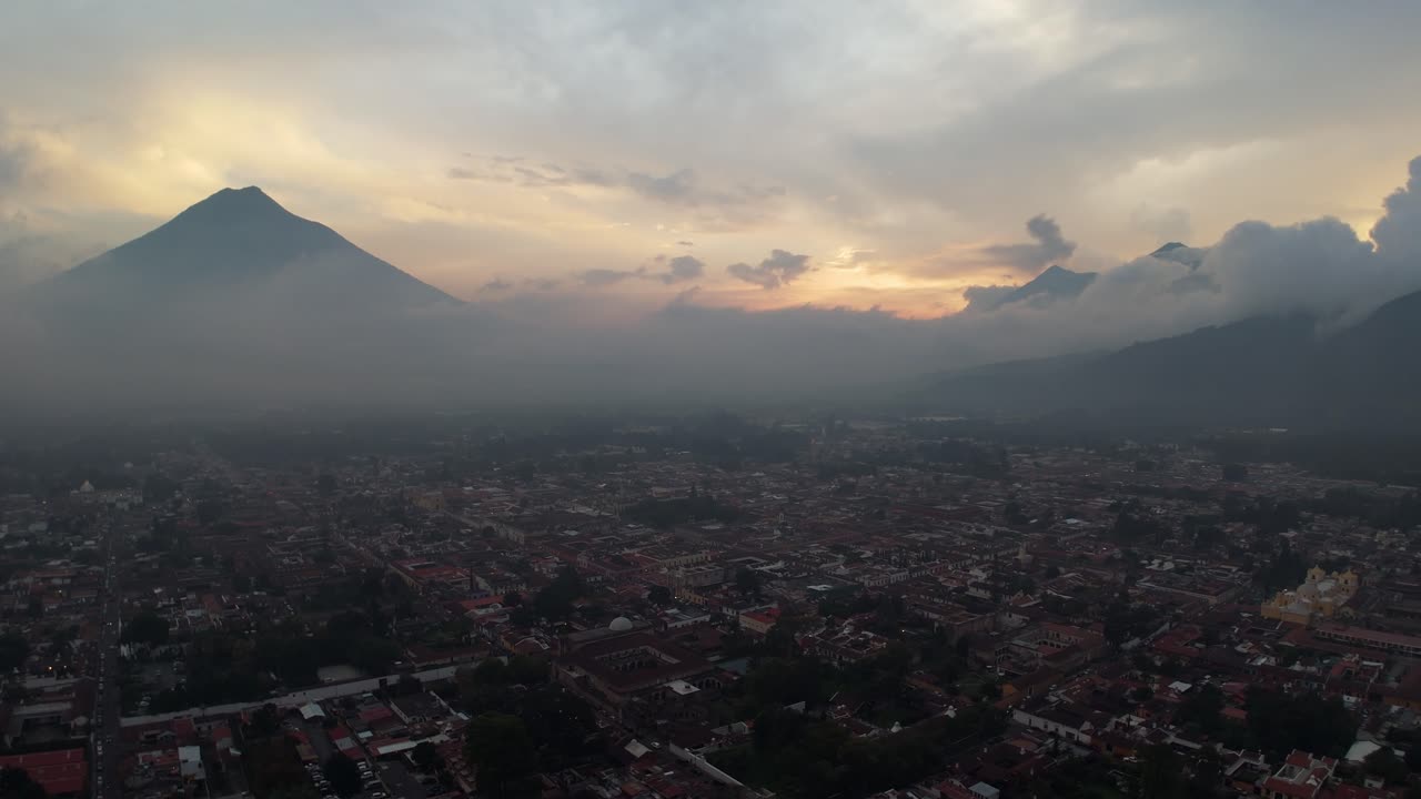 Aerial view over Antigua Guatemala at dusk, with hazy and cloudy sunset sky, Volcan de Agua in background