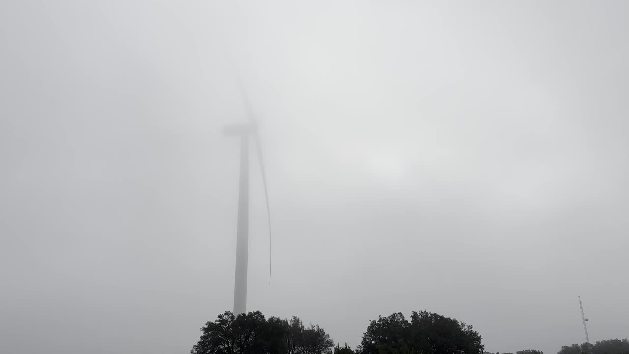 Wind turbine spinning gently in the morning low clouds