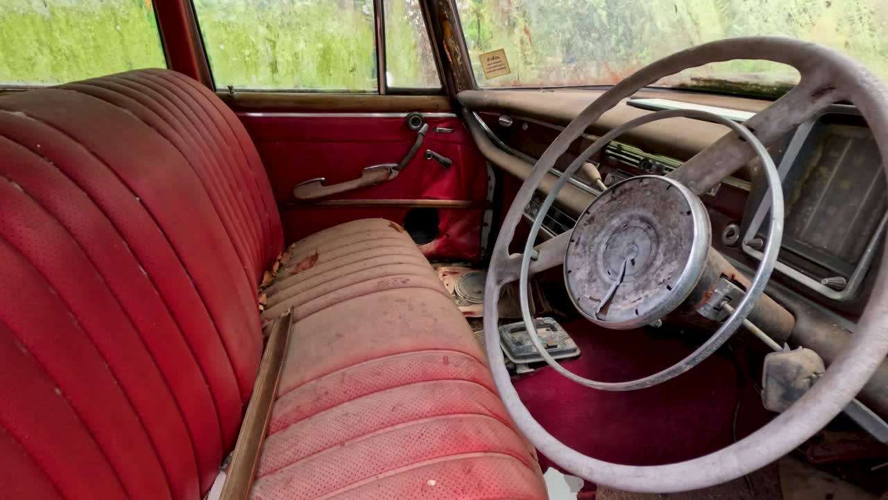 Camera moves from exterior to interior, revealing weathered vintage car with red seats, natural daylight