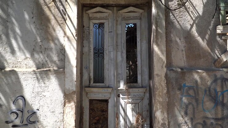 Primo piano di una porta di legno in una casa tradizionale abbandonata nel centro storico di Ioannina, con la luce che crea ombre interessanti.
