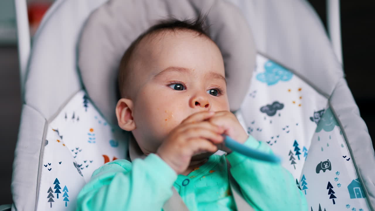 Sweetheart boy in rocking chair chews the spoon. Infant baby after being fed. Close up.