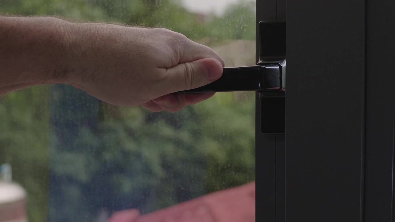 Close up of a man grasping the latch of an aluminum household window, pulling it shut and locking it to secure the home from the inside