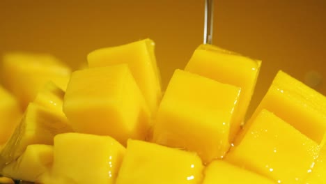 Macro-shot-of-water-falling-into-fresh-Slice-mango-cubes,-Slow-motion