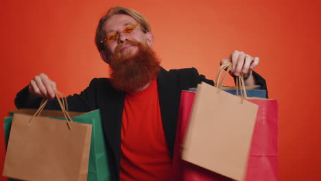 hombre turista feliz mostrando bolsas de compras, promocionando descuentos de vacaciones, asombrado por los bajos precios