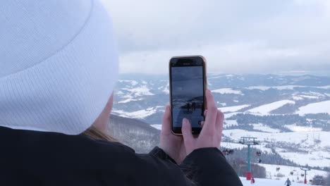 a woman takes photos of a snowy landscape with her smartphone girl shoots video on smartphone on a background of snowy mountains