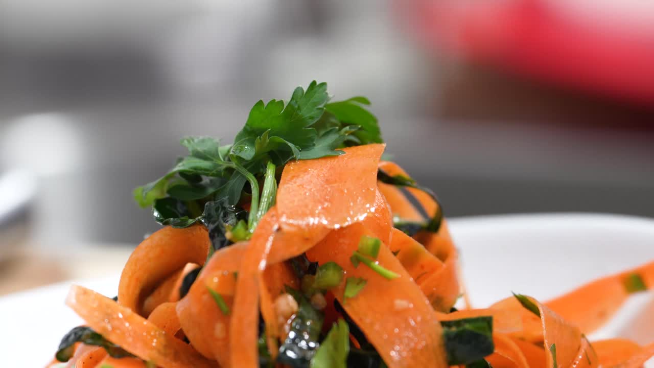 Fresh Parsley Sprig Slowly Placed on Top of Orange Colored Pasta Noodles Infused with Tomato Paste, Carrots or Chickpeas for Garnish by Chef for Lunch or Dinner, Closeup in Restaurant or Home Kitchen