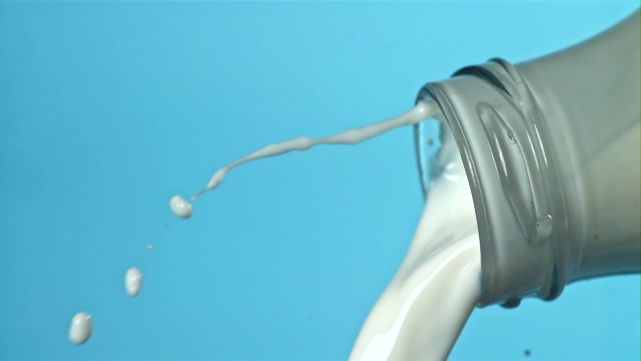 Leite branco derramando de garrafa de vidro em fundo azul.