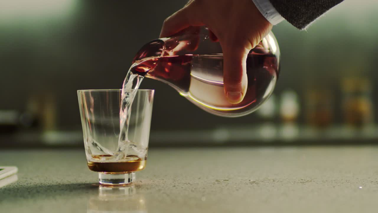 primer plano de la mano masculina vertiendo agua fresca y pura de la jarra en un vaso en la mesa de la cocina.