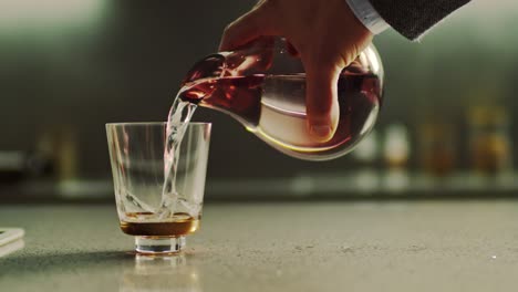 close-up van mannelijke hand die vers puur water uit een kruik in een glas op de keukentafel giet.