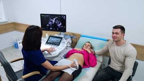 happy couple undergoing the ultrasound pregnancy examination. husband and wife look at their yet unborn baby on the monitor. top view.