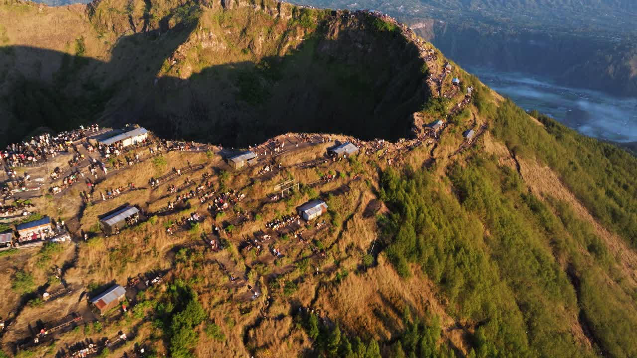 Mount Batur peak with hikers enjoying sunrise, lush green landscape surrounding volcano, crowds of people gather to witness first light across the land