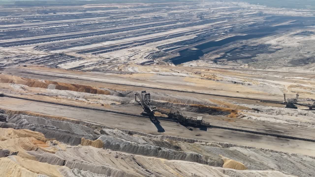 Gigantic excavation machines working in a vast open-cast coal mine on sunny day, aerial orbit