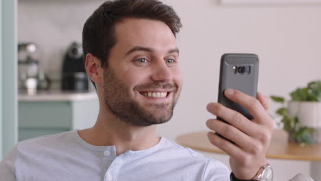 Joven-Feliz-Teniendo-Video-Chat-Usando-Un-Teléfono-Inteligente-Disfrutando-Charlando-En-Línea-Con-Un-Amigo-Relajándose-En-Casa