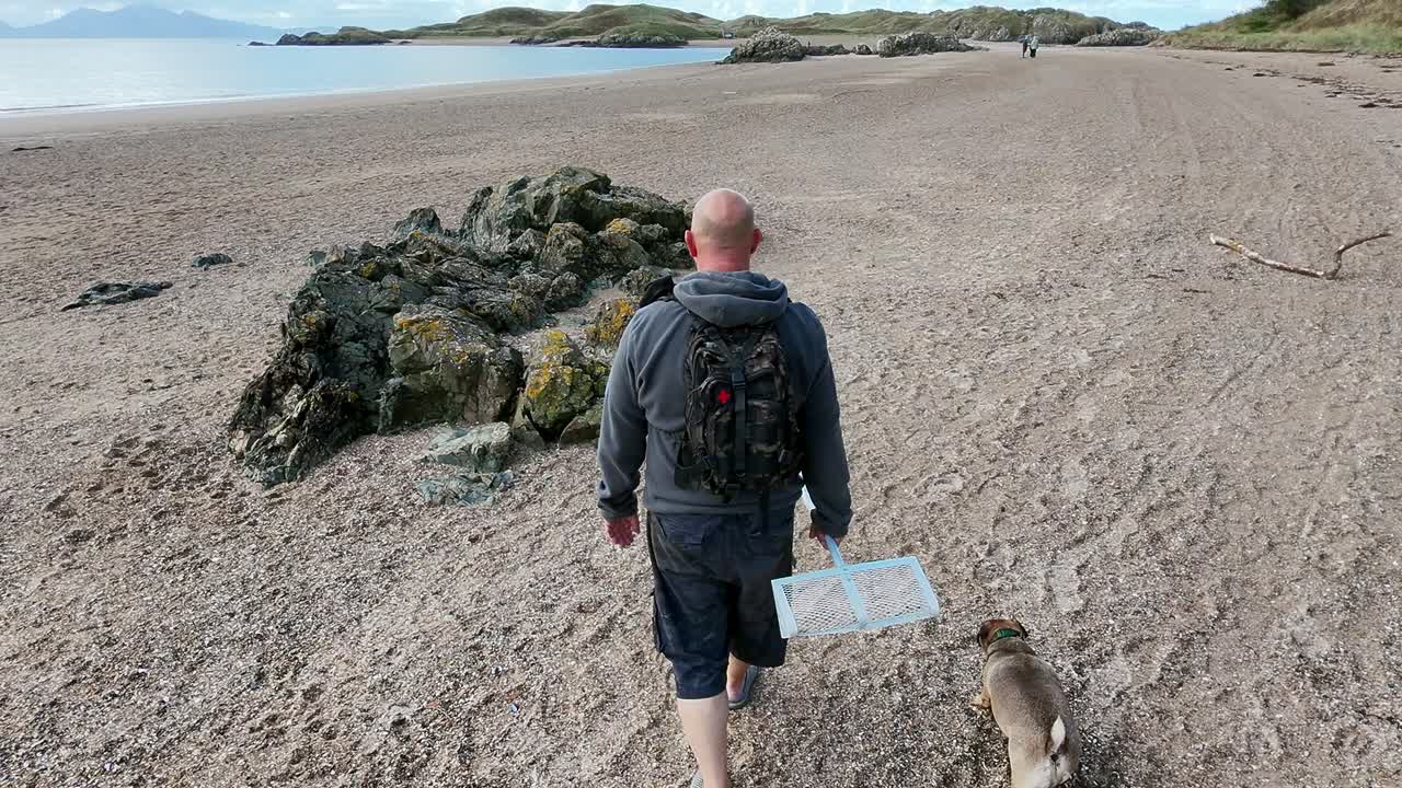 Following active male walking dog between rocks on sandy Welsh beach for early morning exercise