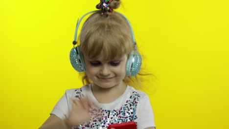 Child-dances-with-smartphone,-listening-to-music-on-headphones.-Little-kid-girl-dancing,-having-hun