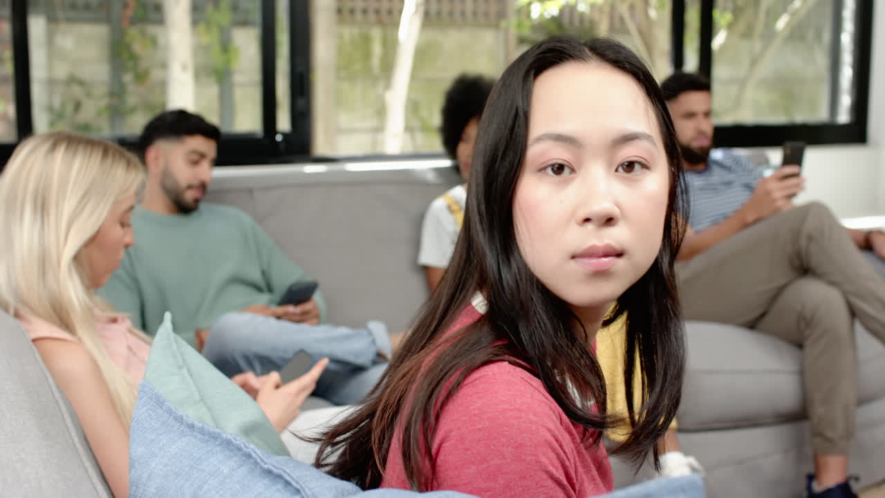 Young woman sitting on couch with friends using smartphones and tablets