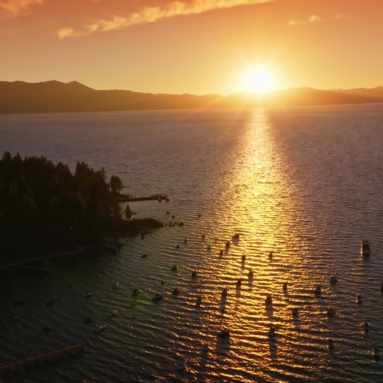 Sailing boats on the water of Lake Tahoe enjoying the stunning sunset. Beautiful scenery of the lake in the rays if setting sun. Mountains at backdrop