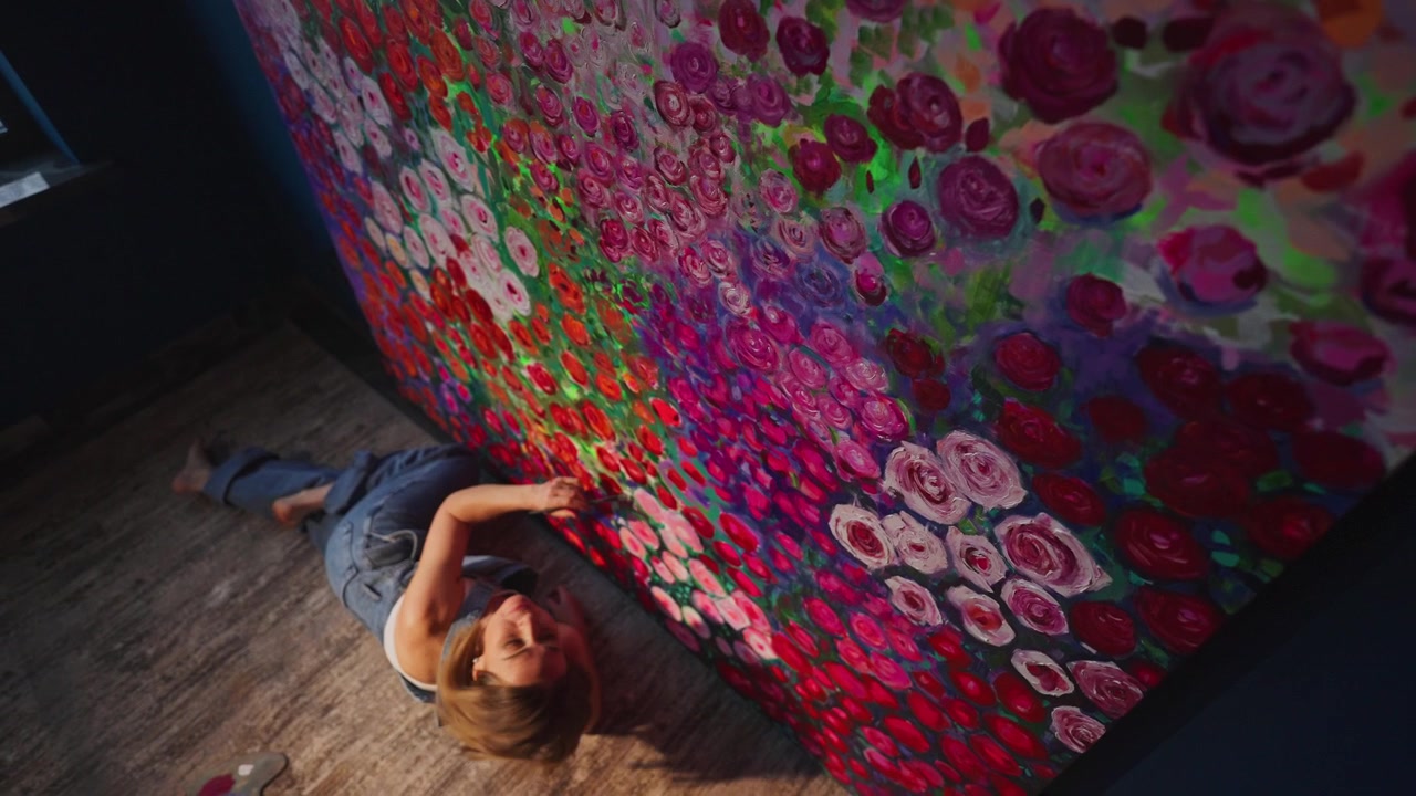 Artista sdraiata sul pavimento mentre dipinge una grande tela floreale