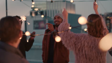 cheerful group of friends holding sparklers celebrating new years eve on rooftop at night having fun dancing enjoying holiday party celebration diverse young people waving festive fireworks