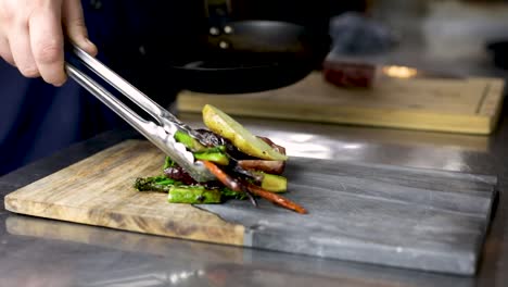 chef plating a healthy seared vegetables by tongs in the kitchen of a restaurant