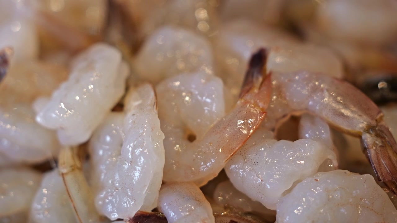 Primo piano di molti gamberi freschi crudi disposti ordinatamente su un vassoio da portata, che mostrano gusci traslucidi, texture naturale e qualità premium dei frutti di mare.