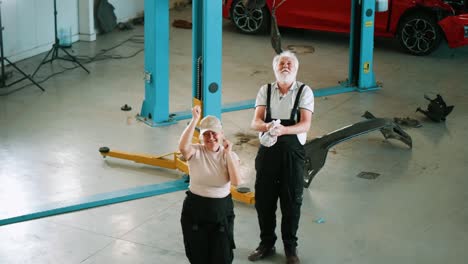 los trabajadores alegres en el servicio de mecánicos de automóviles se divierten bailando al final de las horas de trabajo