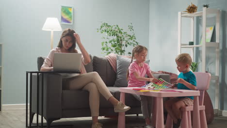 woman works at laptop at home, children next to their mother