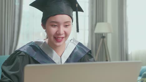 asian woman wearing a graduation gown and cap use laptop computer in living room