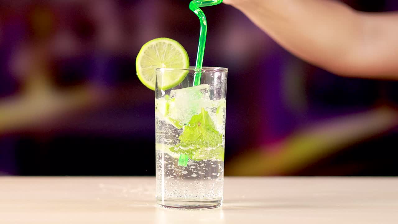 A mojito cocktail is prepared with lime, mint, and a green spiral straw in a vibrant setting