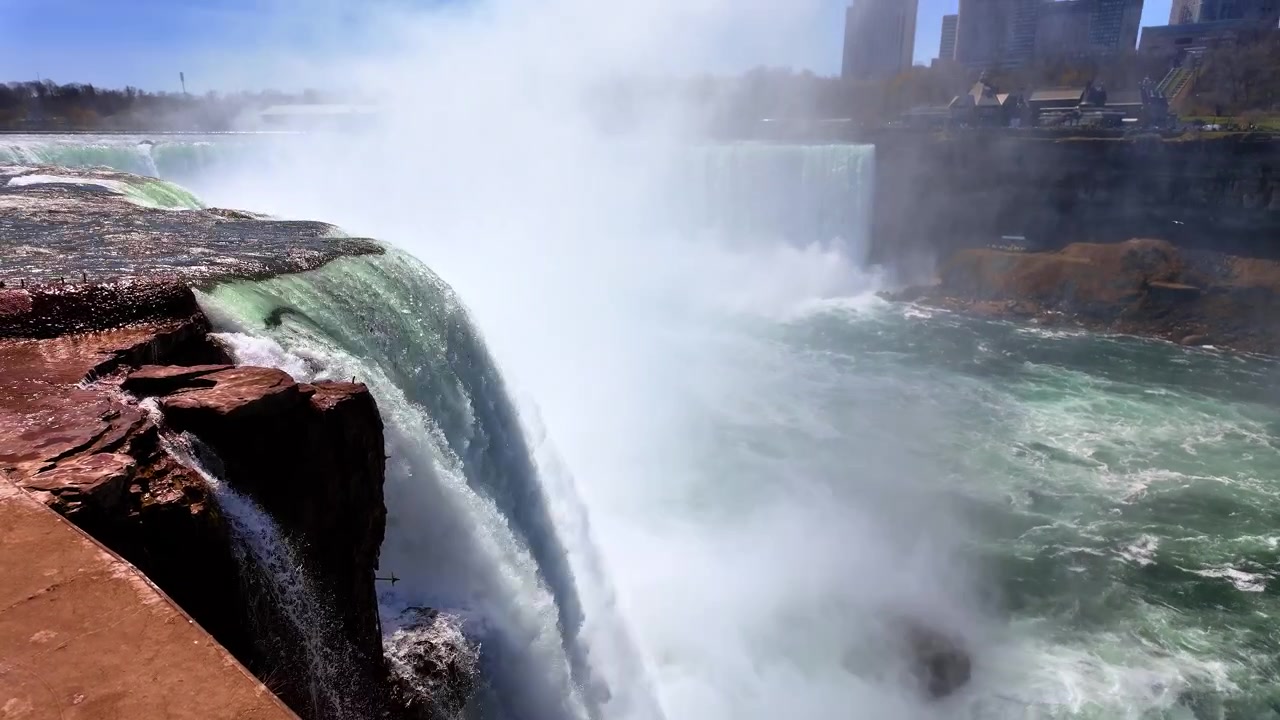 Woda szybko płynie w Wodospadach Niagara w jasnym słońcu w pogodny dzień, ukazując naturalne piękno tego słynnego punktu orientacyjnego. Woda kaskadowo spływa po skałach w Wodospadach Niagara.