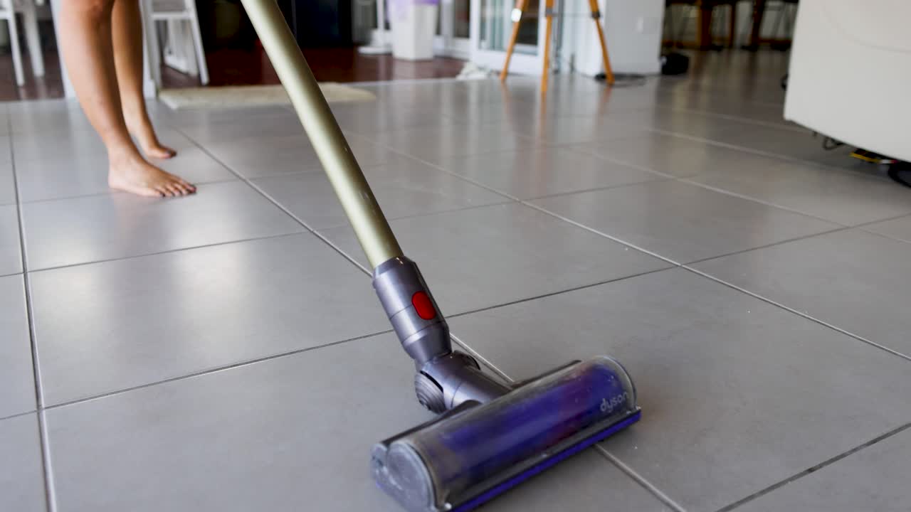 A person vacuums kitchen tiles, focusing on cleanliness and efficiency in a bright, modern home setting