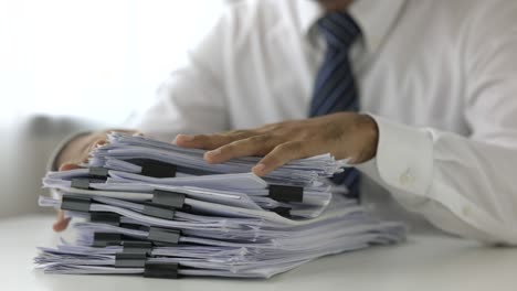 a young business man in a suit is managing paperwork in the office. many paperwork and colorful clip that is not finished.he feeling stressed. documents in the company about finance.