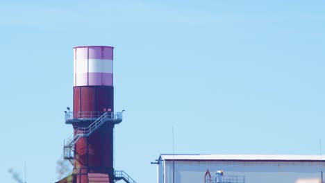 Exterior-view-of-abandoned-Soviet-heavy-metallurgy-melting-factory-Liepajas-Metalurgs-territory,-distant-rust-covered-chimney-and-old-warehouse,-sunny-day,-medium-shot