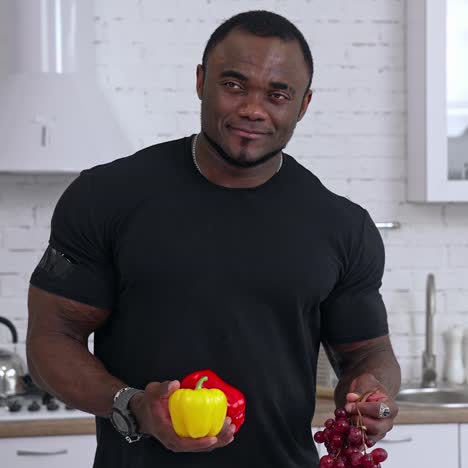 sporty fit african man in the kitchen. black male holding fruit and vegetables in his hands. healthy male offering fresh vegetables