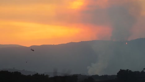 el fuego de thomas arde al atardecer en las colinas sobre ojai california con un helicóptero que cae agua pasando 1