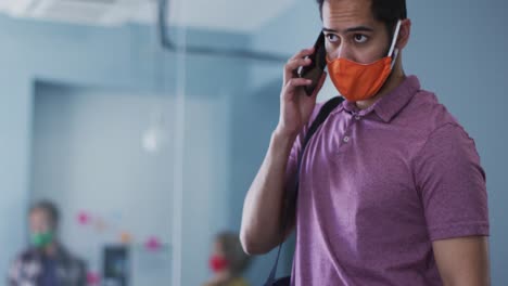 hombre de raza mixta con máscara facial hablando en un teléfono inteligente en la oficina